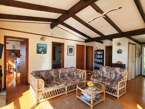 A spacious living room with a large sectional sofa, a coffee table, and a bookshelf. - Classic Kiwi Oceanview Bach (Hahei)