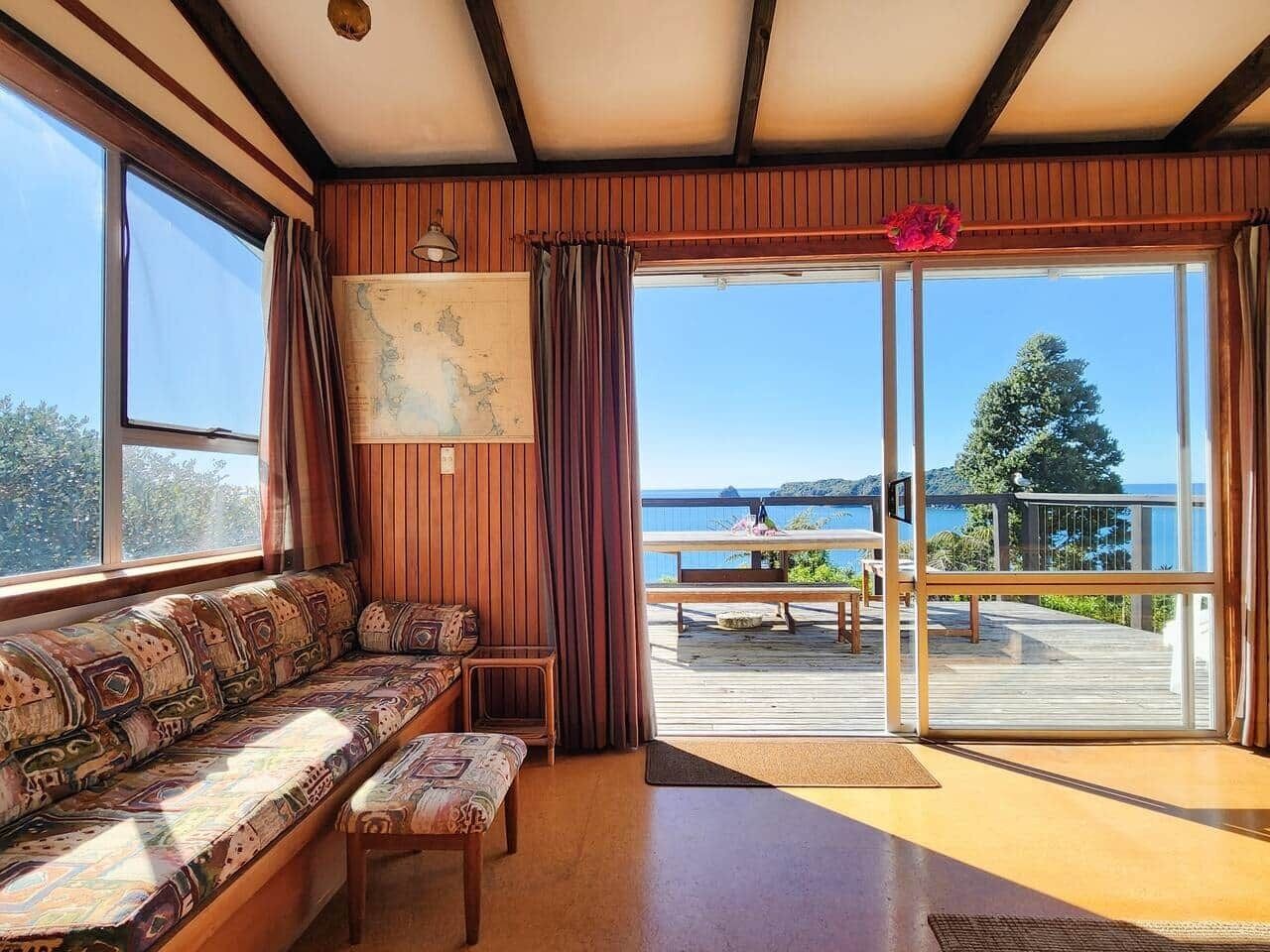 Een kamer met een houten bank, een kaart aan de muur en uitzicht op zee door grote glazen deuren.