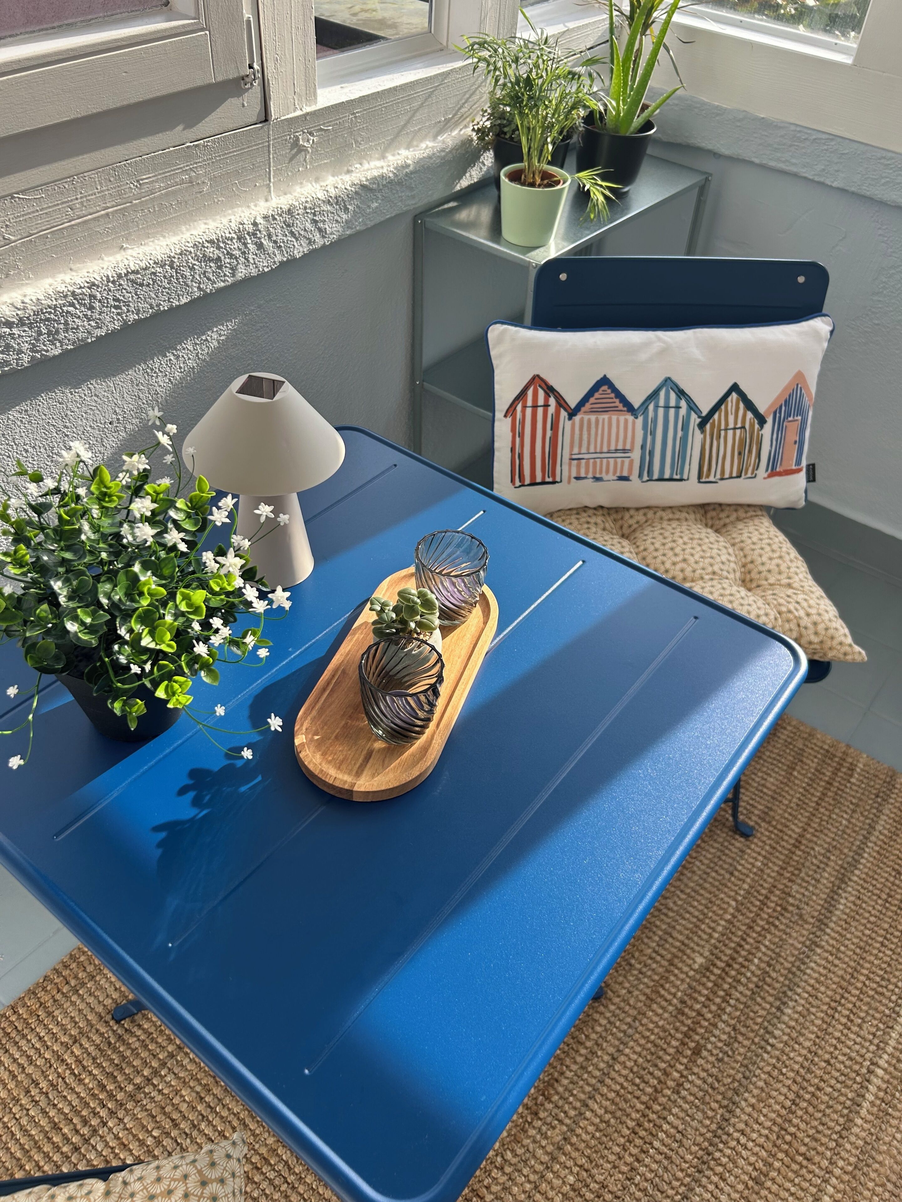 A blue table with a lamp, potted plants, and a tray with decorative items.