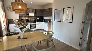 A modern kitchen with a central island, white chairs, and a hanging light fixture.