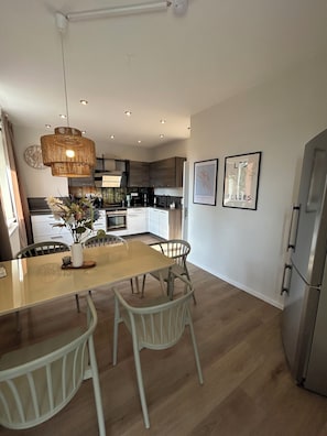 A modern kitchen with a central island, white chairs, and a hanging light fixture.