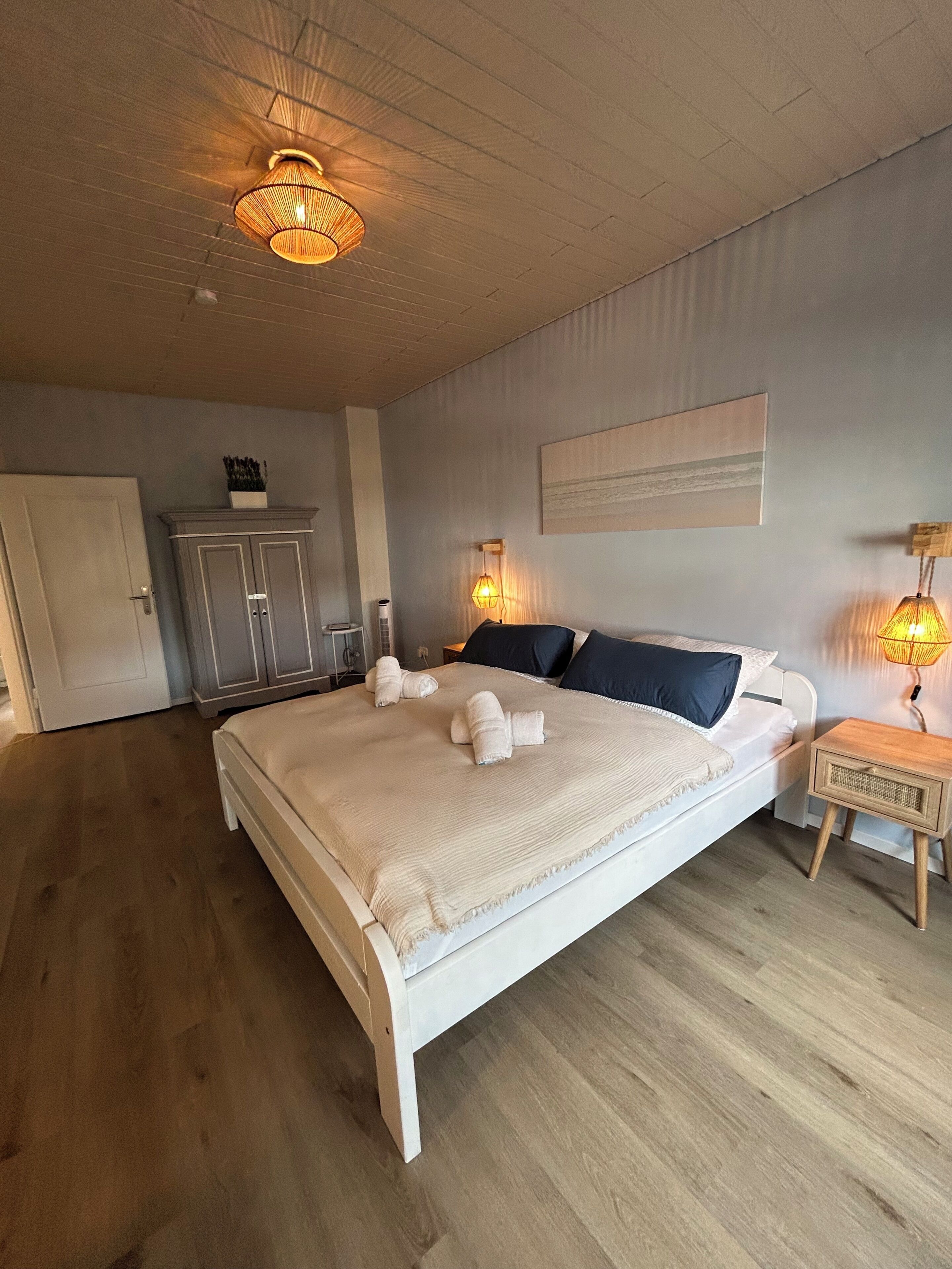 Ein Schlafzimmer mit einem großen Bett, zwei Nachttischlampen, einem Kleiderschrank und einer Tür.