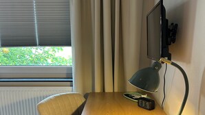 A room with a wooden desk, a chair, a desk lamp, a television, and a window with curtains.
