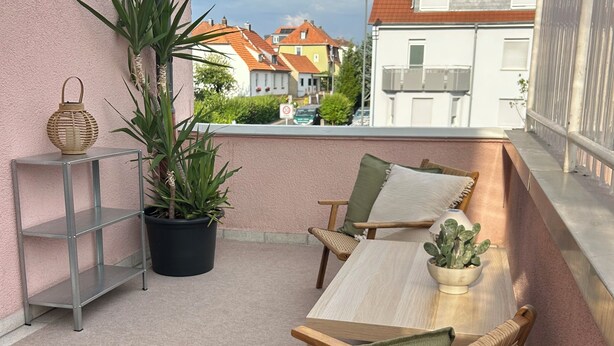 A balcony with wicker furniture, a potted plant, and a view of houses.