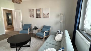 Ein stilvolles Wohnzimmer mit einer Couch, zwei Sesseln, einem Couchtisch und einer Pendelleuchte.