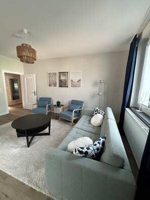 Een moderne woonkamer met een bank, twee fauteuils, een salontafel en een hanglamp.