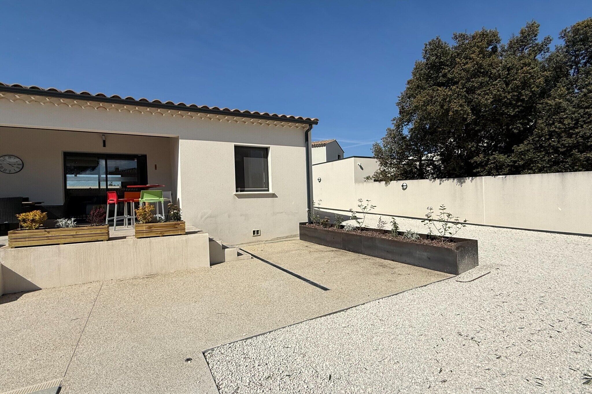 Un bâtiment moderne doté d’un toit plat, d’une petite fenêtre et d’un patio en béton agrémenté d’un jardinier.