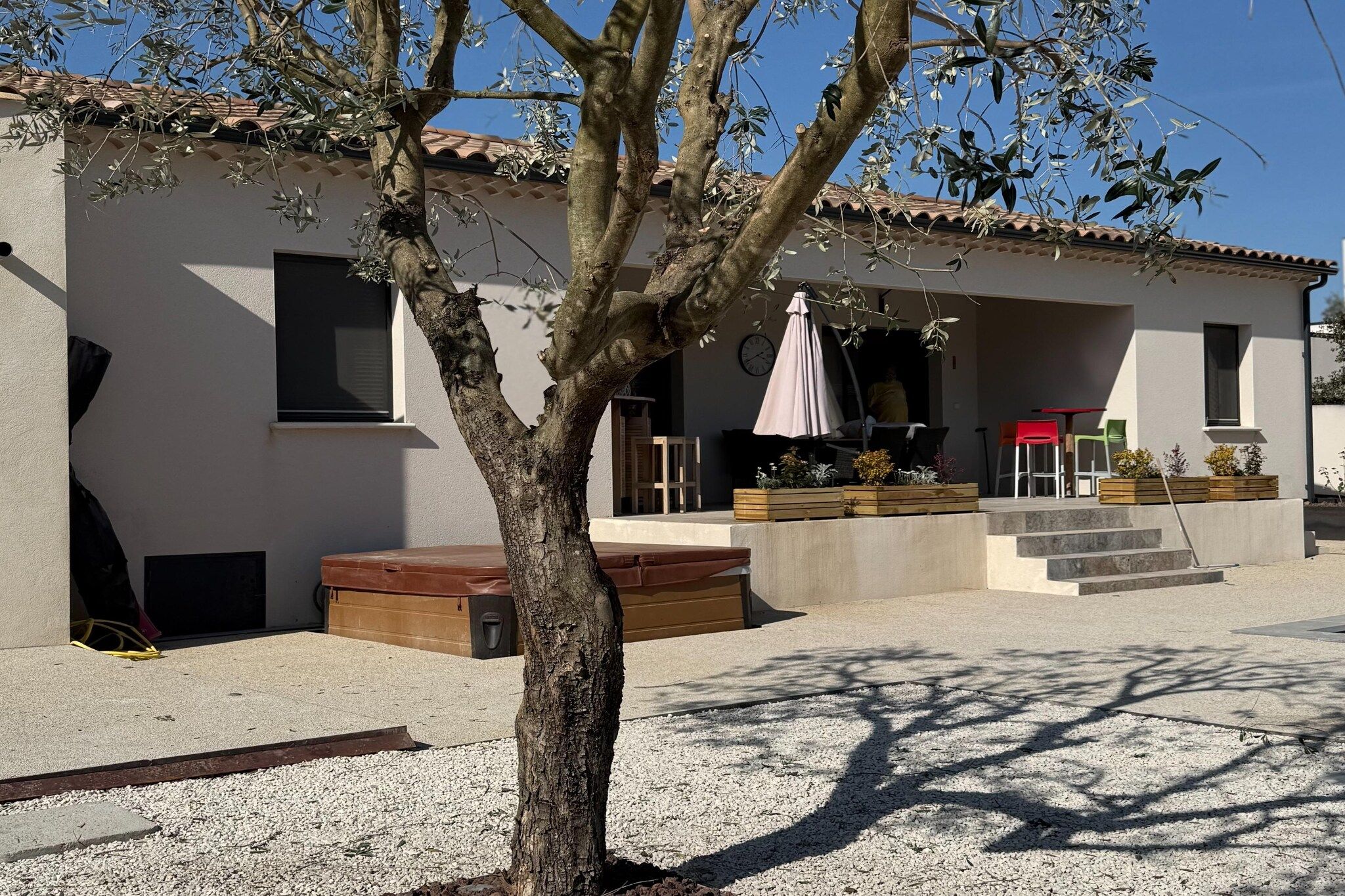 A building with a tiled roof, a tree in front, and outdoor seating with a table and chairs.