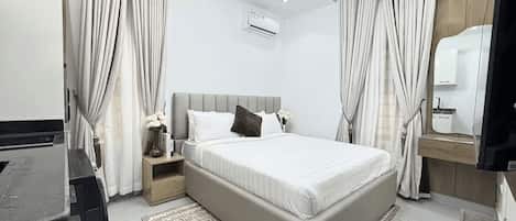 A modern bedroom with a bed, nightstands, a desk, and a mirror.