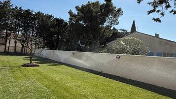 Un área verde con un muro bajo y árboles al fondo.