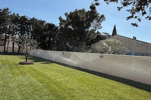 Uma área gramada com um muro baixo e árvores ao fundo.