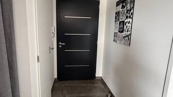 Un pasillo estrecho con una puerta negra, asas horizontales y un felpudo en la entrada.