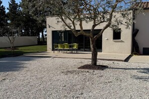 Ein Gebäude mit Kiesterrasse, einem Baum und einer Sitzgelegenheit mit Stühlen.