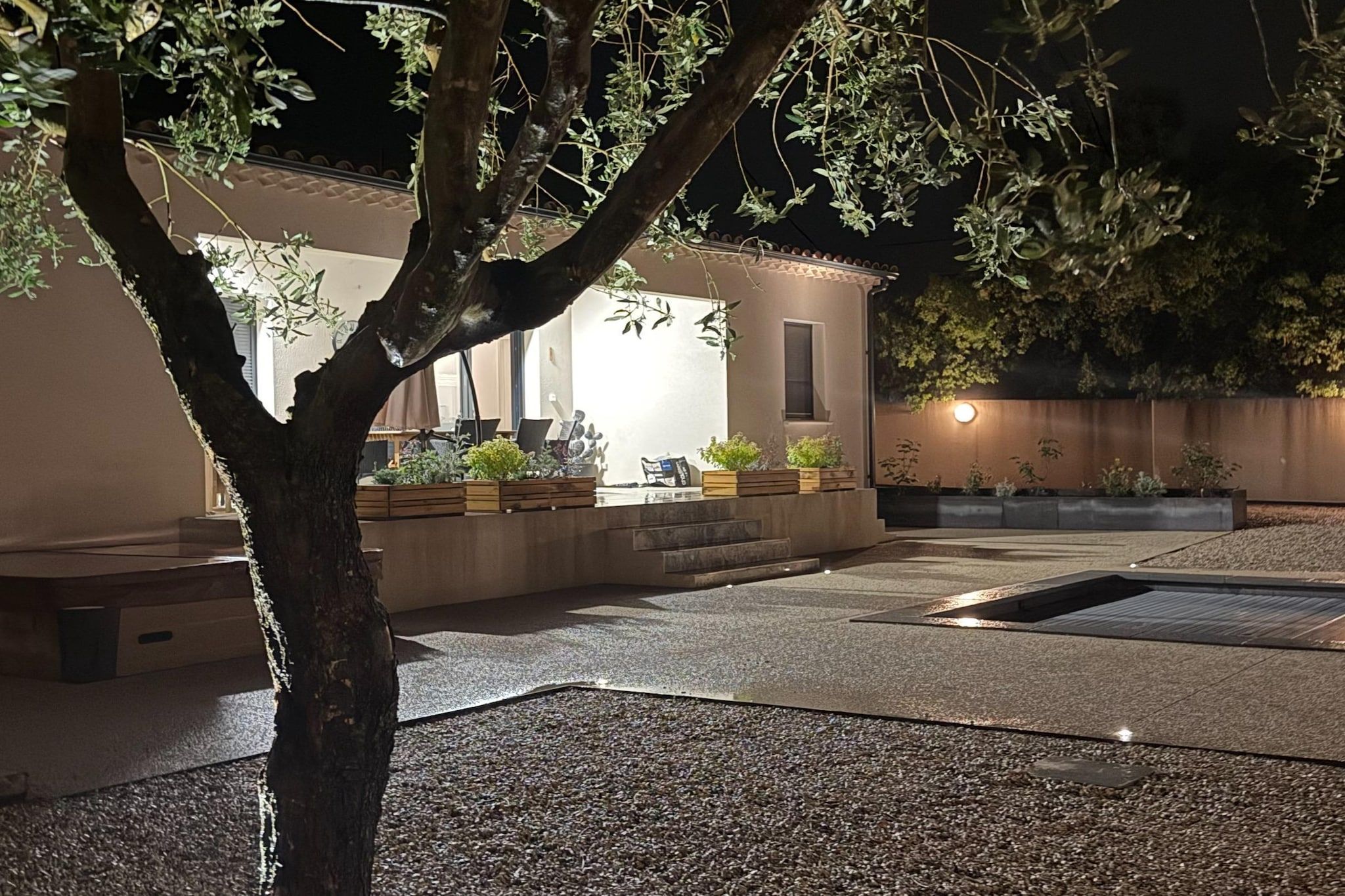 Un espace extérieur bien éclairé, agrémenté d’un arbre, de sièges et de jardinières.