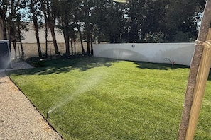 A well-maintained artificial grass lawn with a sprinkler system, surrounded by a white wall and trees. - Villa with pool and jacuzzi near Châteauneuf-du-Pape – 4 people (Sorgues)