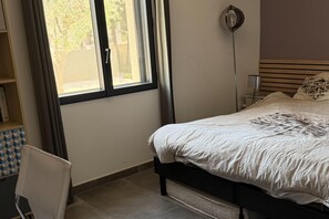 Une chambre à coucher avec un lit, une lampe de chevet, une fenêtre avec des rideaux et une chaise.