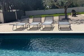 Un espace aménagé au bord de la piscine, comprenant quatre chaises longues et un barbecue.