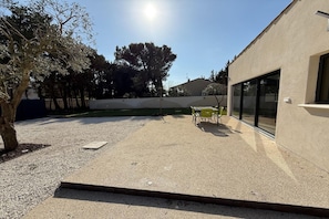A patio area with a table and chairs, a tree, and a building with large windows. - Villa with pool and jacuzzi near Châteauneuf-du-Pape – 4 people (Sorgues)
