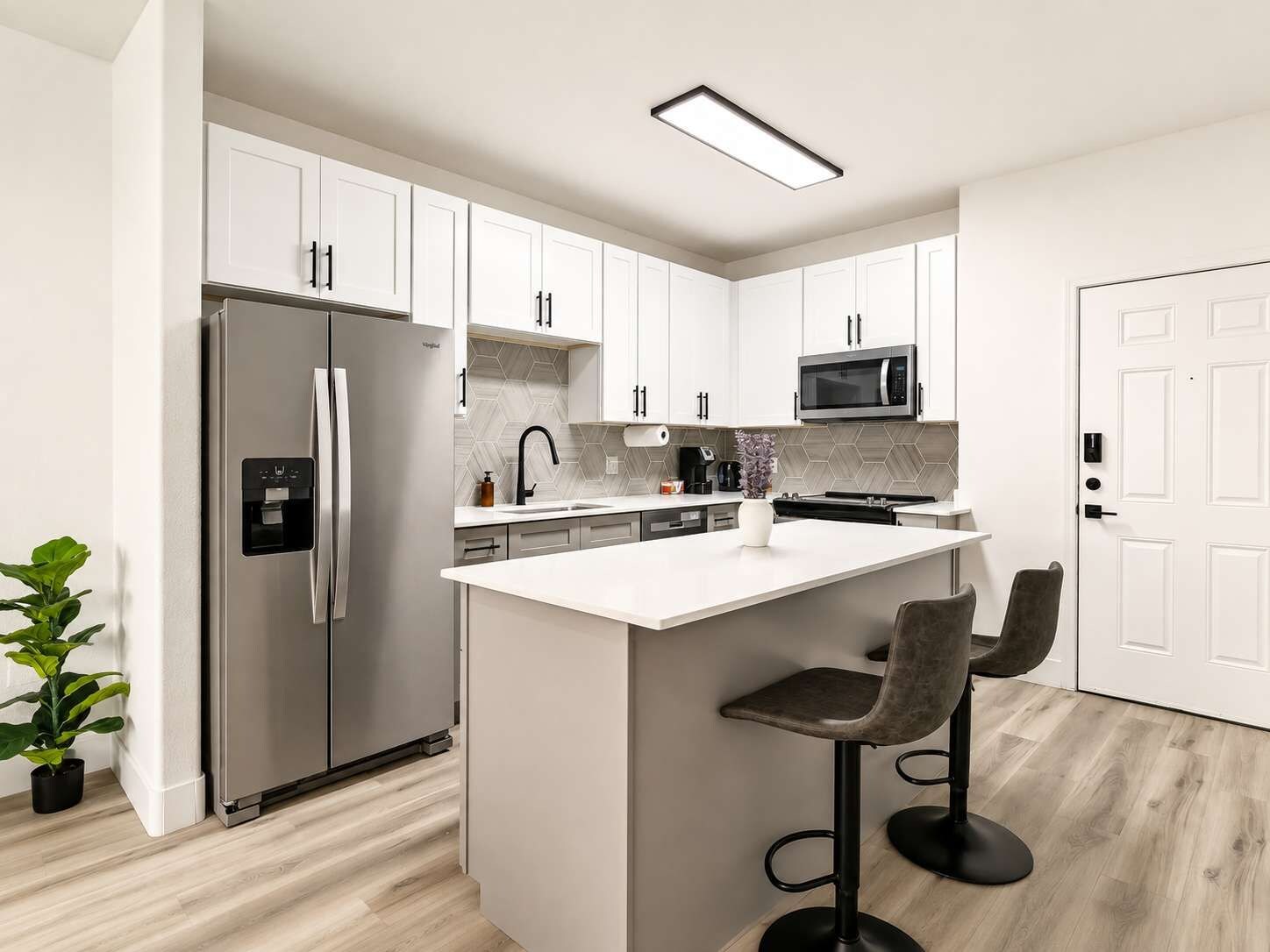 A modern kitchen with white cabinets, a stainless steel refrigerator, a microwave, and a bar stool.