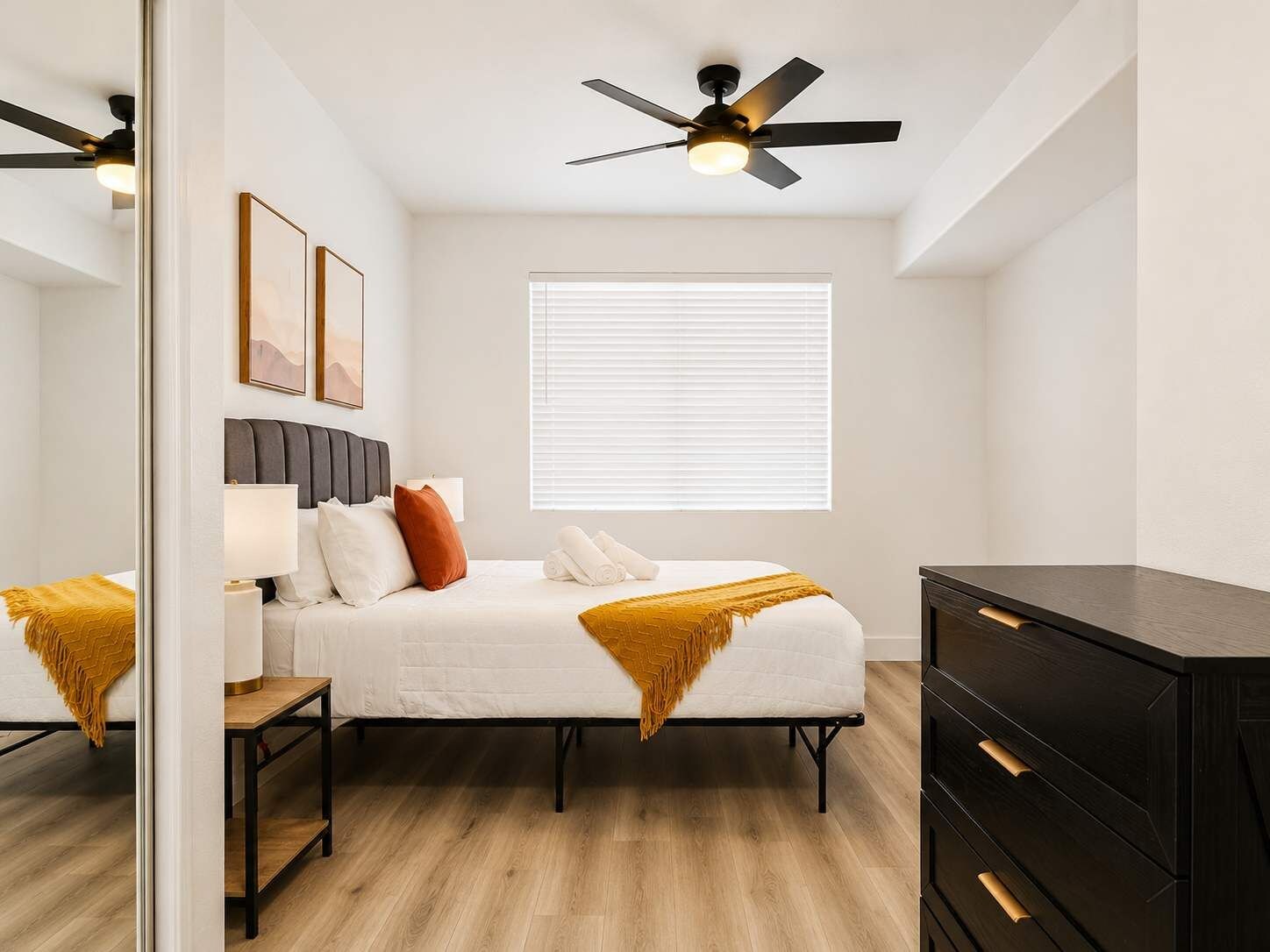 A bedroom with a bed, bedside tables, a dresser, a ceiling fan, and a window with blinds.
