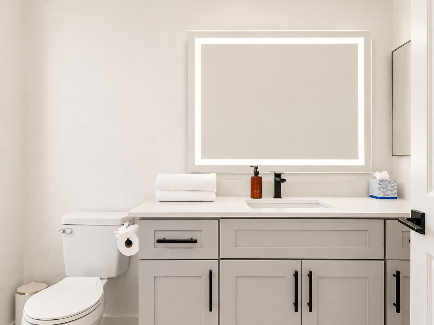 Un baño moderno con inodoro, lavamanos, espejo y armarios.