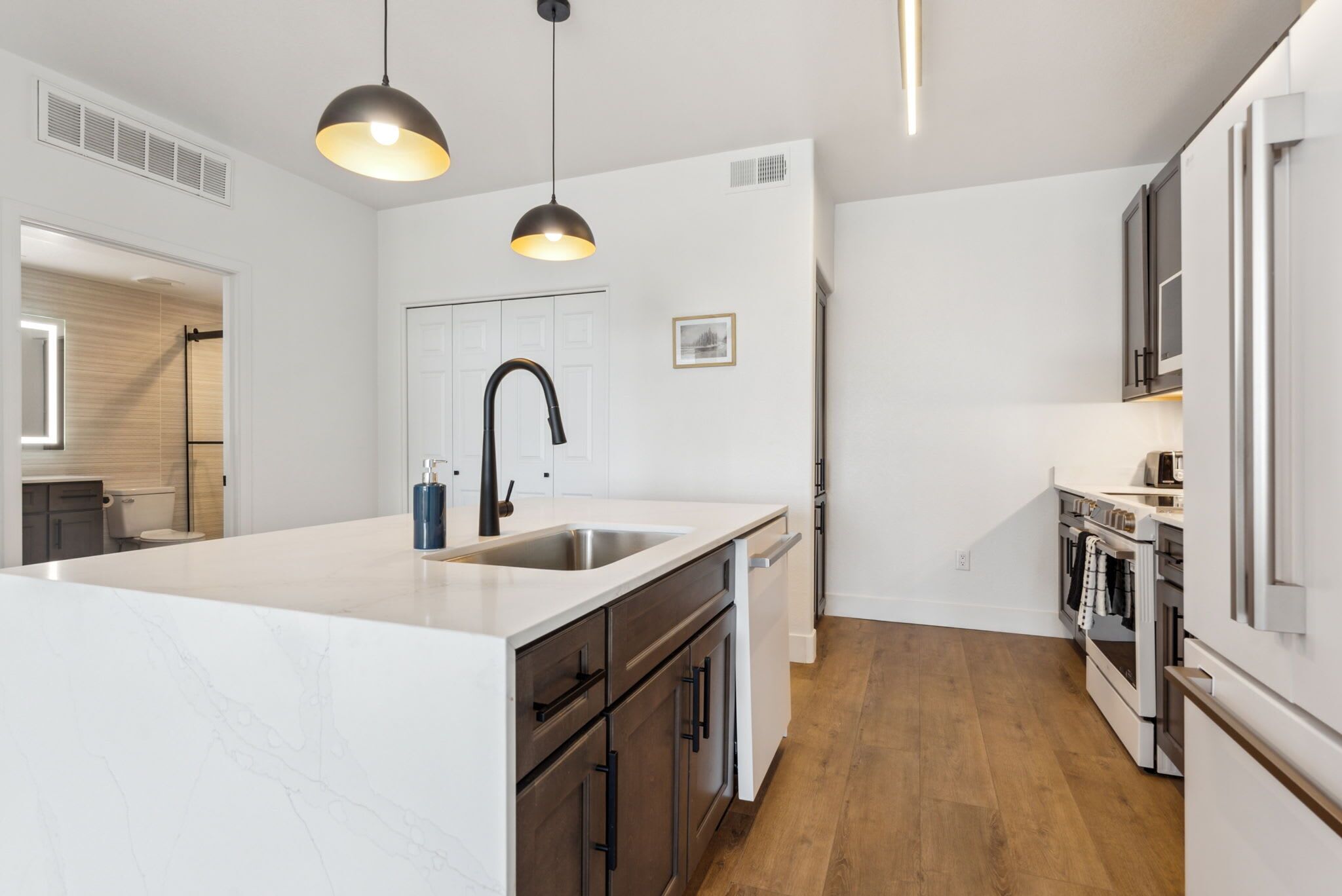 A modern kitchen with a central island, white cabinetry, and a stainless steel sink.