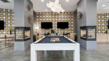A modern indoor pool table with a geometric patterned wall in the background, a flat-screen TV mounted above it, and a minimalist ceiling design.