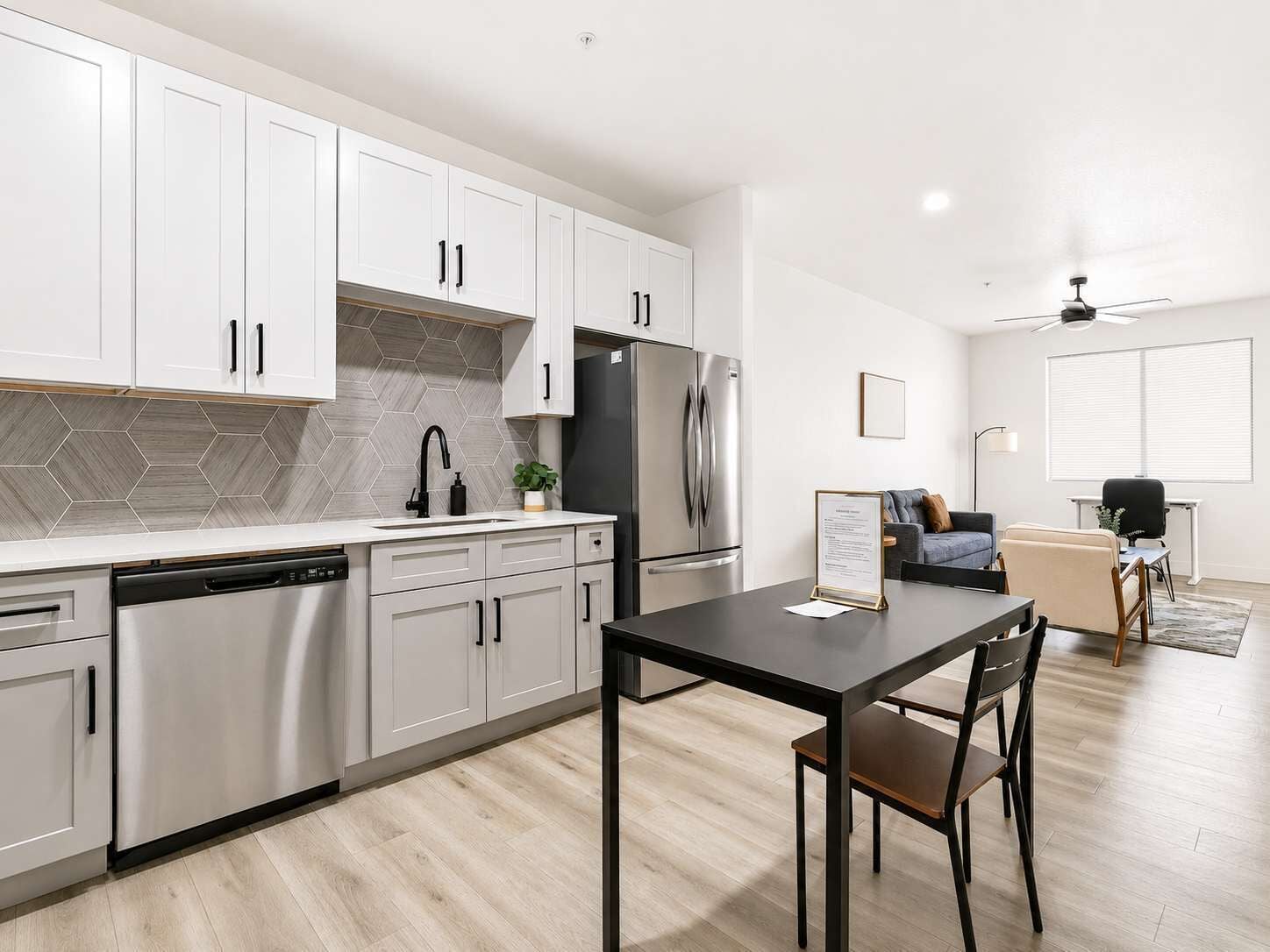 A modern kitchen with white cabinets, a stainless steel refrigerator, and a dining area with a table and chairs.