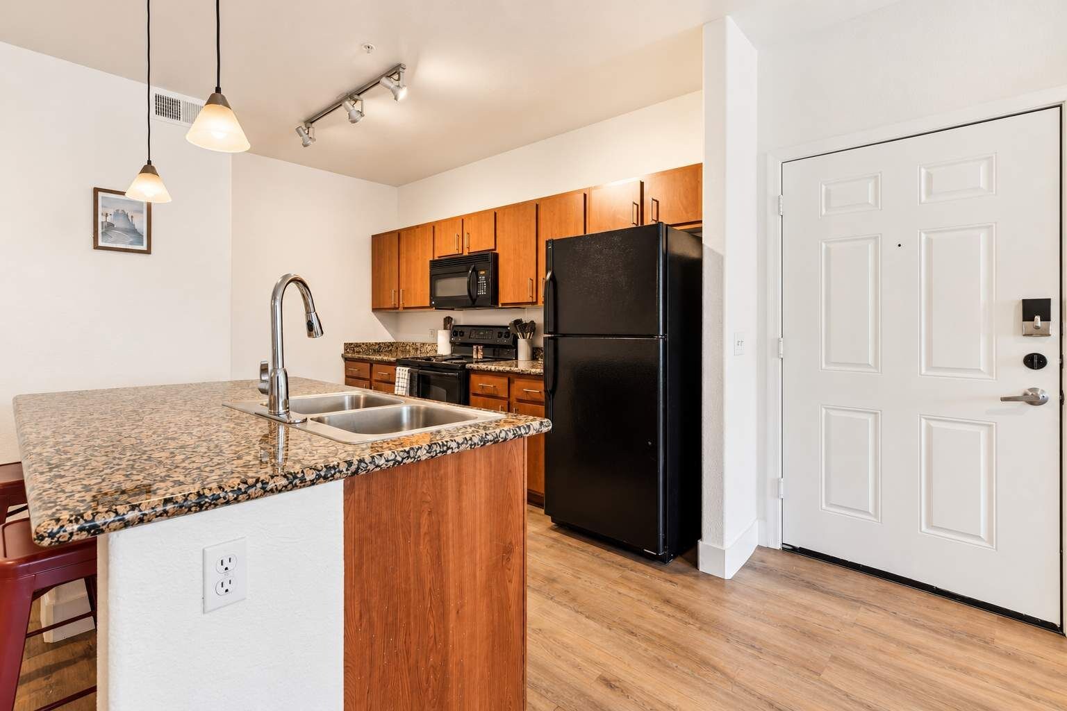 A kitchen with granite countertops, wooden cabinets, a black refrigerator, and a microwave.