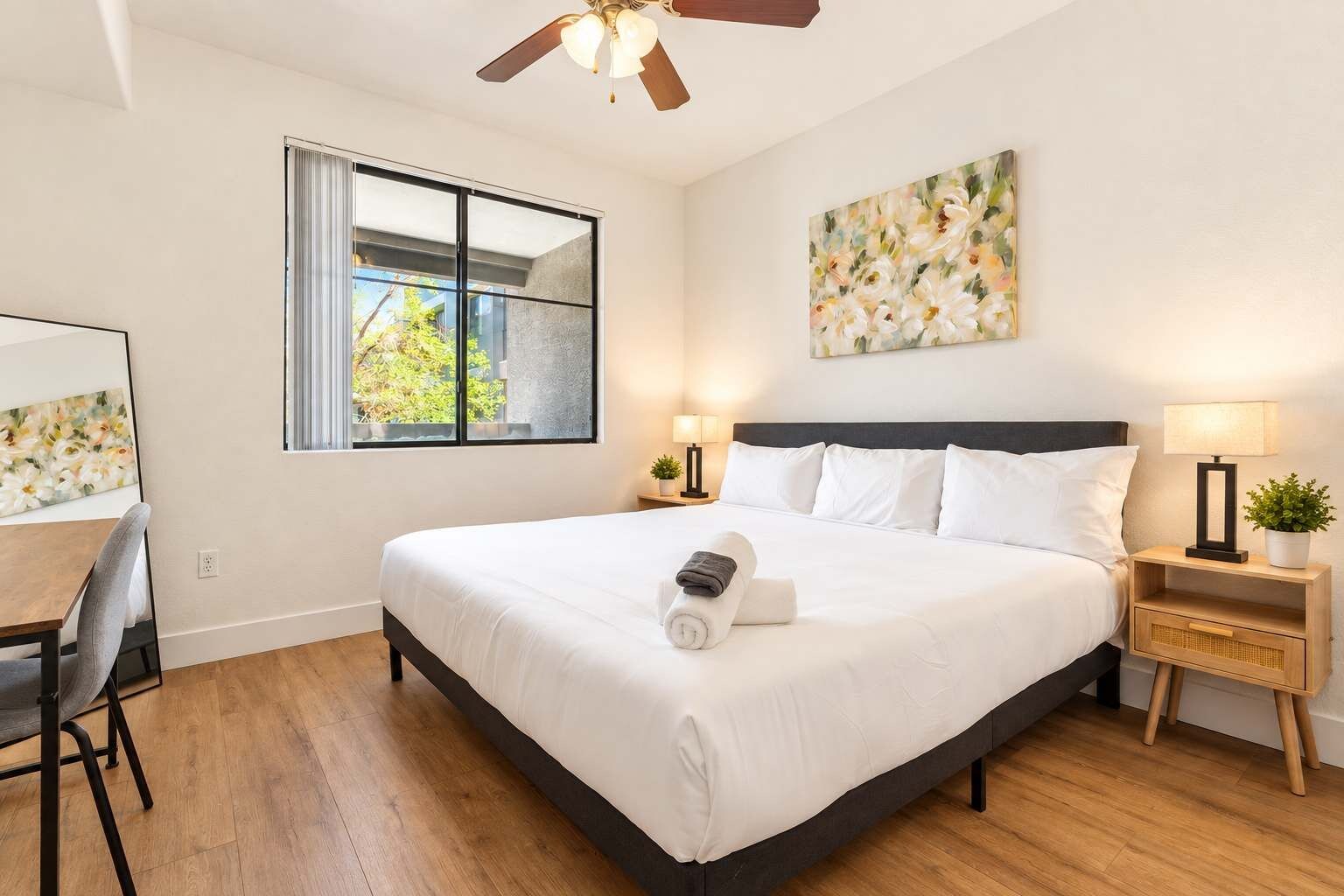 Une chambre d’hôtel avec un grand lit, un bureau, une chaise, une fenêtre donnant sur un beau paysage et un ventilateur de plafond.