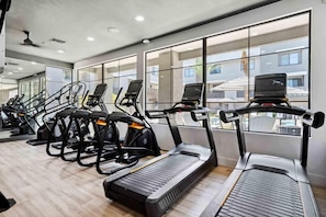 Een sportschool met loopbanden en trainingsfietsen, grote ramen en een modern interieur.
