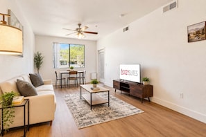 A modern living room with a sofa, coffee table, TV, and a dining area with chairs and a table. - CozySuites Glendale - Westgate w pool! 1BR 1BA (Glendale)