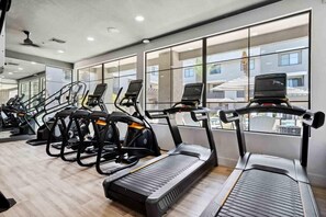 Een sportschool met loopbanden en trainingsfietsen, grote ramen en een modern interieur.