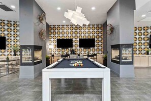 Una mesa de billar moderna en un espacio interior, con un pared decorada con un patrón geométrico, un televisor de pantalla plana montado arriba y un diseño de techo minimalista.