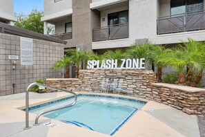 A pool area with a sign reading "SPLASH ZONE," a hot tub, and a stone wall with palm trees. - CozySuites Glendale - Westgate w pool! 1BR 1BA (Glendale)