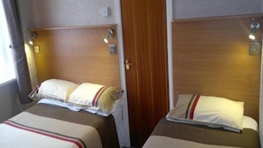 Two single beds with headboards, bedside lamps, and a wooden door between them. - Standard Triple Room (Blackpool)