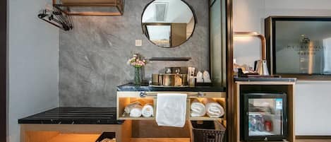 Une salle de bain moderne avec un mur en marbre, un miroir rond, un lavabo avec un porte-serviettes et un petit réfrigérateur.