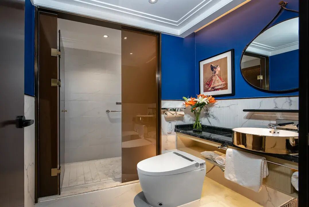 A modern bathroom with a glass shower enclosure, a white toilet, a vanity with a mirror, and a vase of flowers.