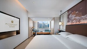 A hotel room with a large bed, a desk, a chair, and a view of the cityscape.