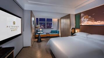 Ein Hotelzimmer mit Bett, Schreibtisch, Stuhl, Sofa, Fernseher und Fenster mit Stadtblick.