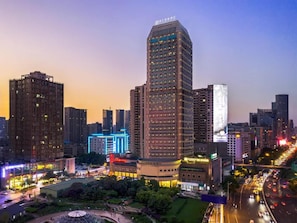 Un paisaje urbano al anochecer con edificios iluminados y una calle concurrida.