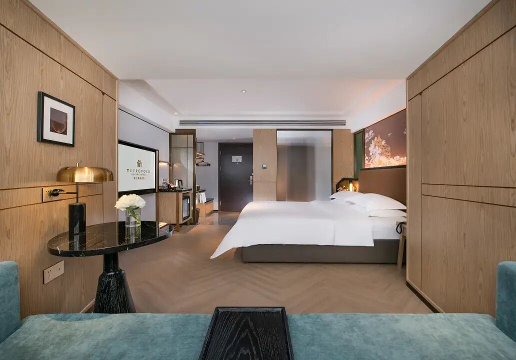 A modern hotel room with a bed, a desk, a chair, and a view of the city.