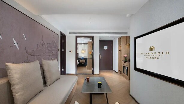 A hotel room with a sofa, a small table, and a wall with a decorative mural.