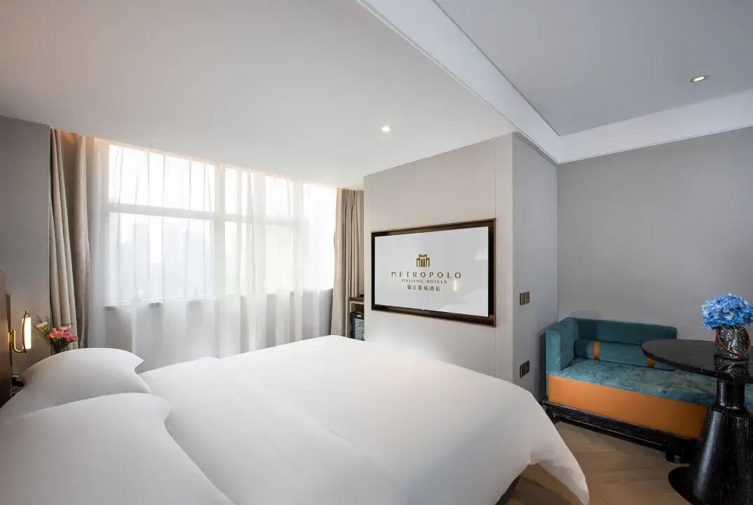 Habitación de hotel con una cama grande, un sofá, una mesita con un florero y un cartel en la pared.