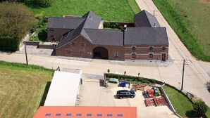 Een gebouw met twee verdiepingen, een bakstenen gevel en een schuin dak, naast een parkeerplaats met een auto en bouwmaterialen.