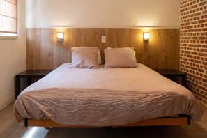A bed with a wooden headboard, two bedside tables, and a brick wall. - Apartment 3 – Enjoy a cozy stay at the Alfonsinehoeve (Horpmaal)