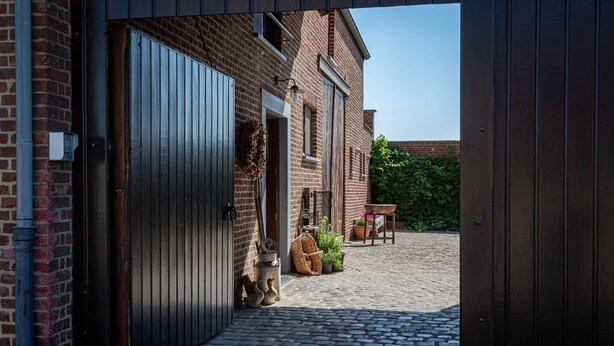 Een gebouw van baksteen met grote metalen deuren, een geplaveid binnenhof en een kleine tafel met stoelen.