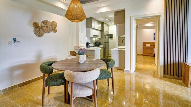 A modern dining area with a round table, green upholstered chairs, and a hanging light fixture. - King Size Bed| PrivateBBQ| CapCana| Beach Juanillo (Punta Cana)