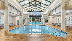 En stor indendørs swimmingpool med højt til loftet og naturligt lys.