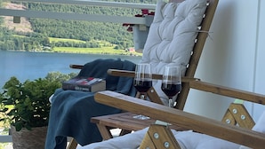 A wooden deck with a lounge chair, a small table, and a hanging flower basket. - Solvang Ferienhaus mit Fjordblick & privatem Garten (Møre og Romsdal)